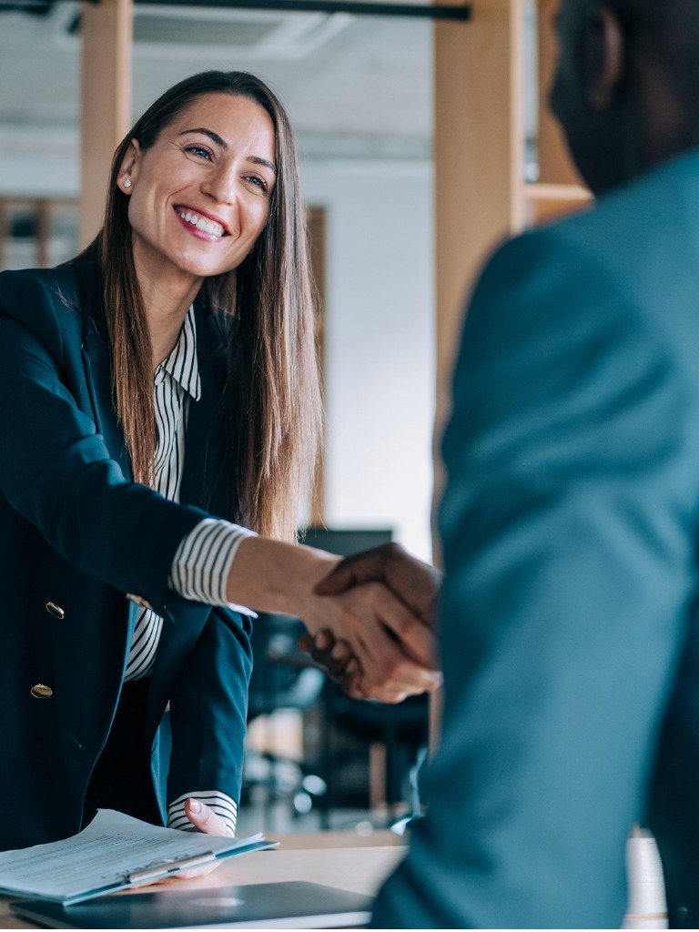 Businesswoman shaking hands with colleague in office, smiling and looking professional.