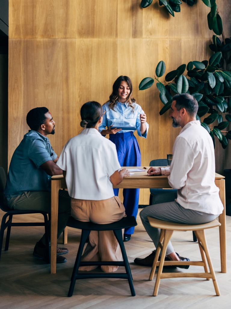 Diverse professionals in a meeting, one presenting on a tablet.
